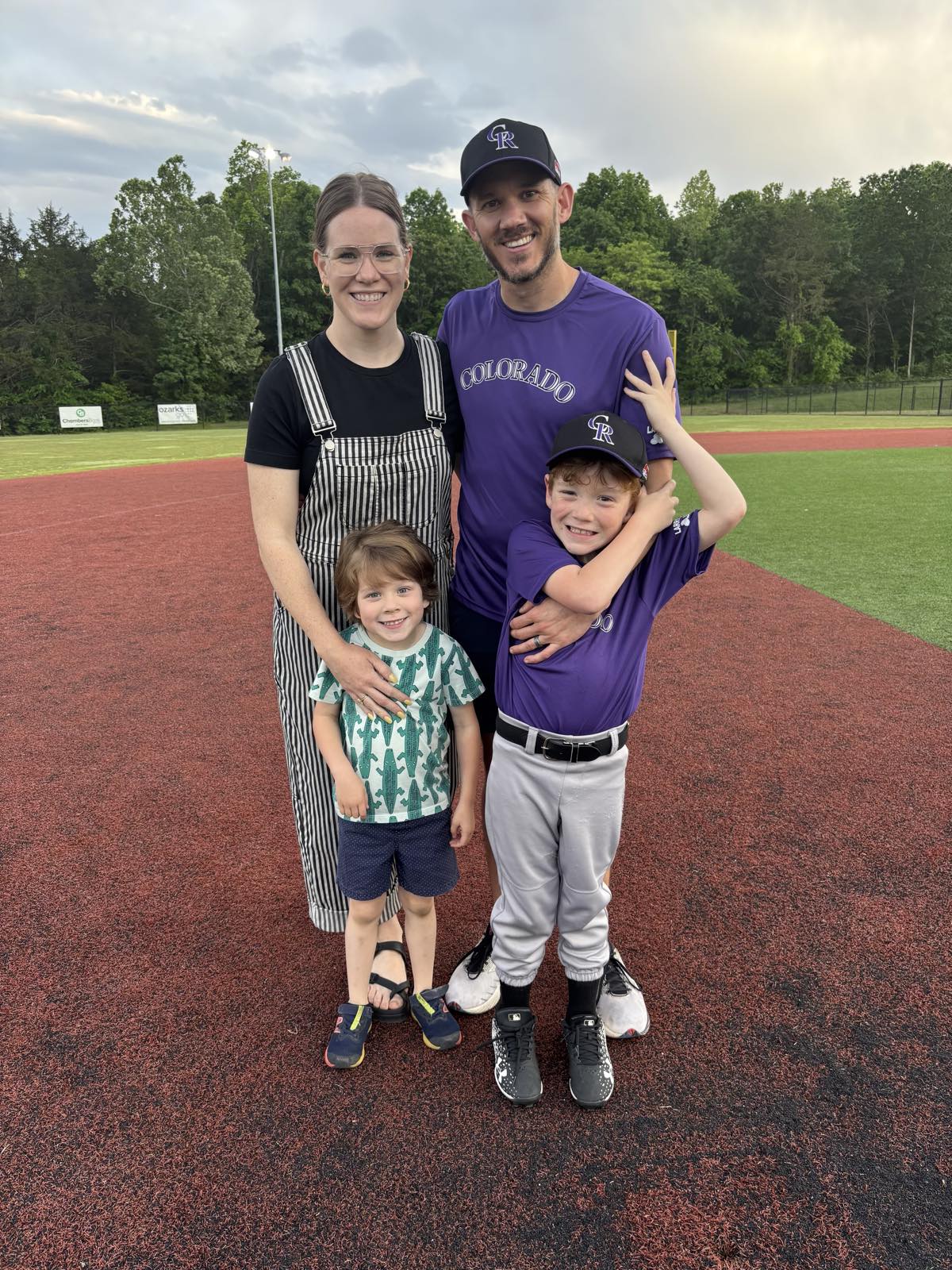 Family of four at a youth baseball field, cheering on a Colorado Rockies-themed team.